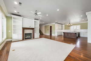 Unfurnished living room with dark wood-type flooring, a glass covered fireplace, visible vents, and crown molding