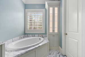 Bathroom featuring ornamental molding, marble finish floor, and a garden tub