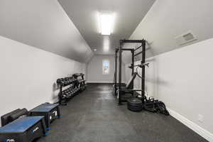 Exercise room featuring baseboards, visible vents, and vaulted ceiling