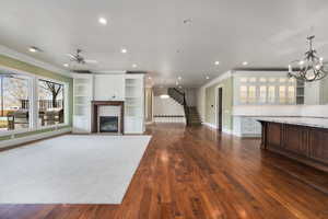 Unfurnished living room featuring dark wood-style floors, stairs, crown molding, and a glass covered fireplace