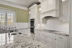 Kitchen with black electric stovetop, decorative backsplash, double oven, glass insert cabinets, and ornamental molding