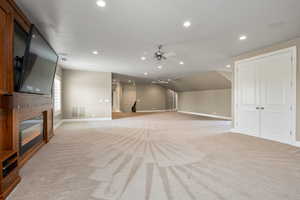 Unfurnished living room with light carpet, recessed lighting, baseboards, and a glass covered fireplace