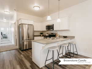 Kitchen with stainless steel appliances, a peninsula, visible vents, white cabinets, and a kitchen breakfast bar