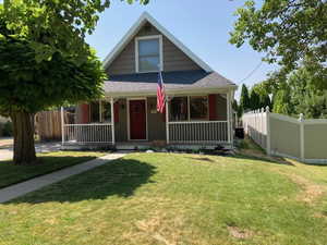 Bungalow-style home featuring roof with shingles, fence, a porch, and a front yard