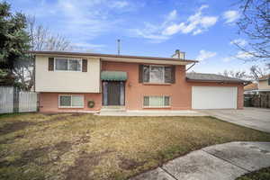 Bi-level home featuring a chimney, fence, a garage, driveway, and a front lawn