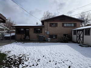 Snow covered rear of property with an outbuilding, central AC, brick siding, and a storage shed