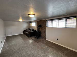 Unfurnished living room with a wood stove, carpet, baseboards, and a textured ceiling