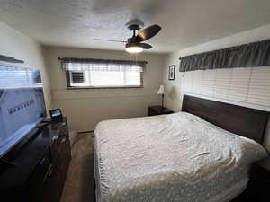 Bedroom with a textured ceiling, dark colored carpet, and ceiling fan