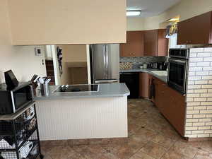 Kitchen with backsplash, a peninsula, light countertops, black appliances, and a sink