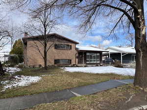 View of front of property with brick siding, a chimney, a sunroom, fence, and a carport