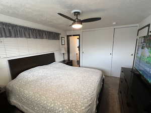 Carpeted bedroom featuring a textured ceiling, ceiling fan, and a closet