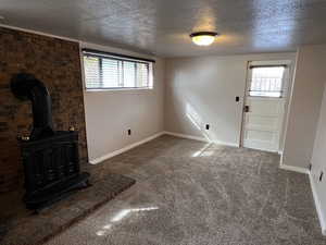 Unfurnished living room with a textured ceiling, carpet floors, plenty of natural light, and a wood stove