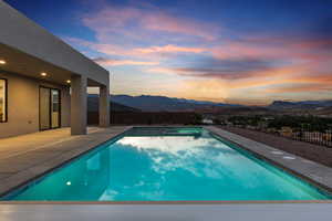 Pool at dusk with a mountain view, a fenced backyard, a patio area, and a pool with connected hot tub
