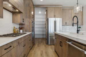 Kitchen with appliances with stainless steel finishes, extractor fan, backsplash, light wood finished floors, and light stone counters