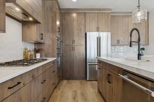 Kitchen featuring stainless steel appliances, exhaust hood, light wood finished floors, tasteful backsplash, and light stone counters