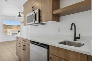 Kitchen featuring stainless steel appliances, open shelves, ceiling fan, light countertops, and light wood-type flooring