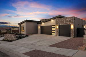 Contemporary house featuring an attached garage, concrete driveway, stone siding, and a mountain view