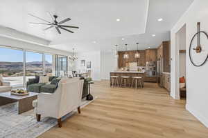 Living area with light wood-type flooring, recessed lighting, ceiling fan, a chandelier, and a tray ceiling
