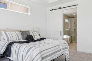 Bedroom with a barn door, light tile patterned flooring, light colored carpet, and connected bathroom
