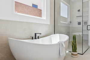 Full bath featuring tile patterned flooring, a shower stall, a freestanding tub, and tile walls