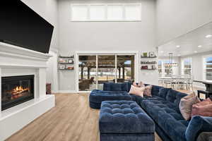 Living area with a glass covered fireplace, baseboards, a towering ceiling, and light wood finished floors