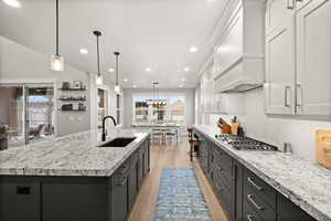 Kitchen featuring white cabinets, light wood-style floors, premium range hood, stainless steel gas stovetop, and a sink