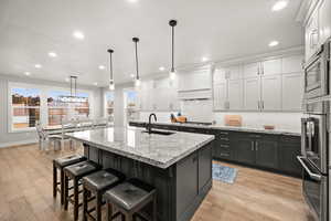 Kitchen with light wood finished floors, a center island with sink, appliances with stainless steel finishes, custom exhaust hood, and a sink