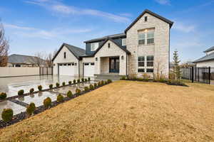 View of front of house featuring a garage, fence, concrete driveway, stone siding, and a front lawn