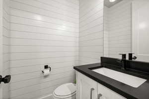 Half bath with wood walls, vanity, and toilet