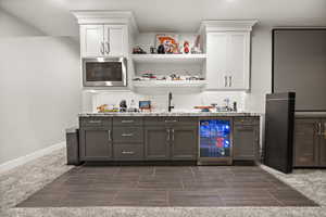 Bar with wine cooler, indoor wet bar, stainless steel microwave, decorative backsplash, and baseboards