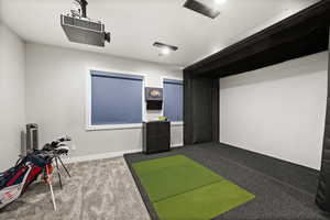 Game room with dark colored carpet, golf simulator, and baseboards