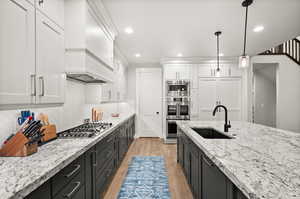 Kitchen with white cabinets, custom exhaust hood, stainless steel appliances, light wood-type flooring, and a sink