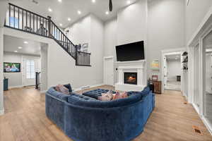 Living area with light wood-type flooring, visible vents, a glass covered fireplace, and a towering ceiling