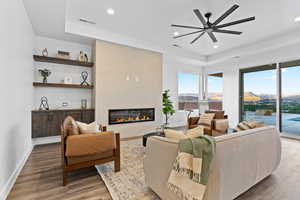 Living area featuring a tray ceiling, wood finished floors, a ceiling fan, a tile fireplace, and recessed lighting