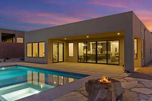 Back of house at dusk featuring an outdoor fire pit, a patio, a pool with connected hot tub, and stucco siding