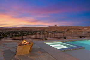 Pool at dusk with a fire pit, an in-ground hot tub, a mountain view, a fenced backyard, and a patio
