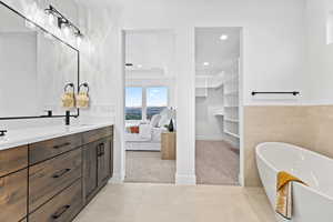 Ensuite bathroom featuring a soaking tub, double vanity, a walk in closet, and recessed lighting