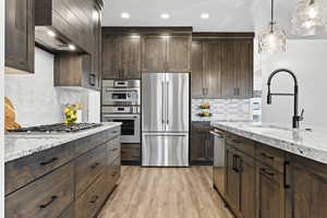 Kitchen featuring appliances with stainless steel finishes, exhaust hood, dark brown cabinets, light stone countertops, and recessed lighting