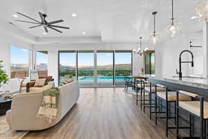 Living room with wood finished floors, a tray ceiling, recessed lighting, ceiling fan, and a chandelier