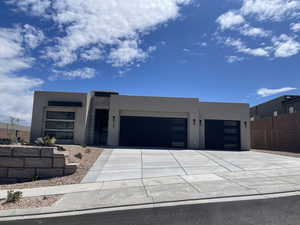 Contemporary home with stucco siding, an attached garage, driveway, and fence