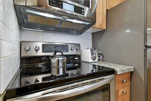 Kitchen featuring appliances with stainless steel finishes, brown cabinets, light stone counters, and tasteful backsplash