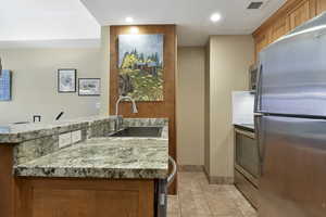 Kitchen featuring light tile patterned floors, stainless steel appliances, a sink, visible vents, and brown cabinetry