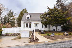 Cape cod house featuring a garage, driveway, and fence