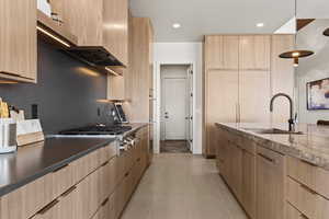 Kitchen with light brown cabinets, a sink, ventilation hood, modern cabinets, and dark stone counters