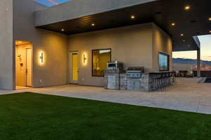 Patio terrace at dusk featuring a yard, outdoor wet bar, and area for grilling