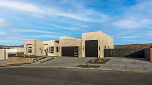 View of front facade with a garage, driveway, fence, and stucco siding