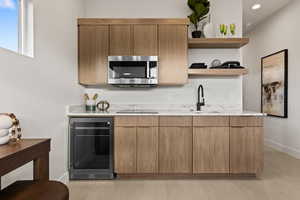 Kitchen with beverage cooler, stainless steel microwave, black electric cooktop, open shelves, and a sink