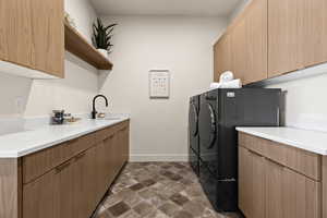 Laundry area featuring independent washer and dryer, a sink, cabinet space, and baseboards