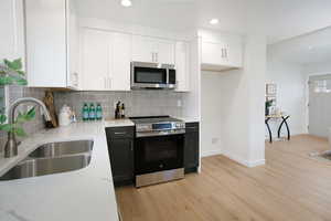 Kitchen with white cabinets, light wood-style flooring, appliances with stainless steel finishes, light stone countertops, and a sink