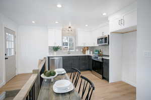 Kitchen featuring stainless steel appliances, light countertops, white cabinets, a sink, and light wood-type flooring